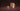 Five chocolate bars in colorful packaging stand upright between two red mineral rocks. Unwrapped pieces of white and dark chocolate are stacked on the left, all set against a dark brown background. - AI generated text