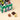 A festive green box of assorted Venchi chocolates beside a Vintage Dream winter cottage, with three signature pieces. - AI generated text