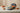 A round gift box with a floral pattern and orange ribbon sits open on a table, revealing assorted wrapped chocolates. Two small, orange gift boxes with bows are also on the table. - AI generated text